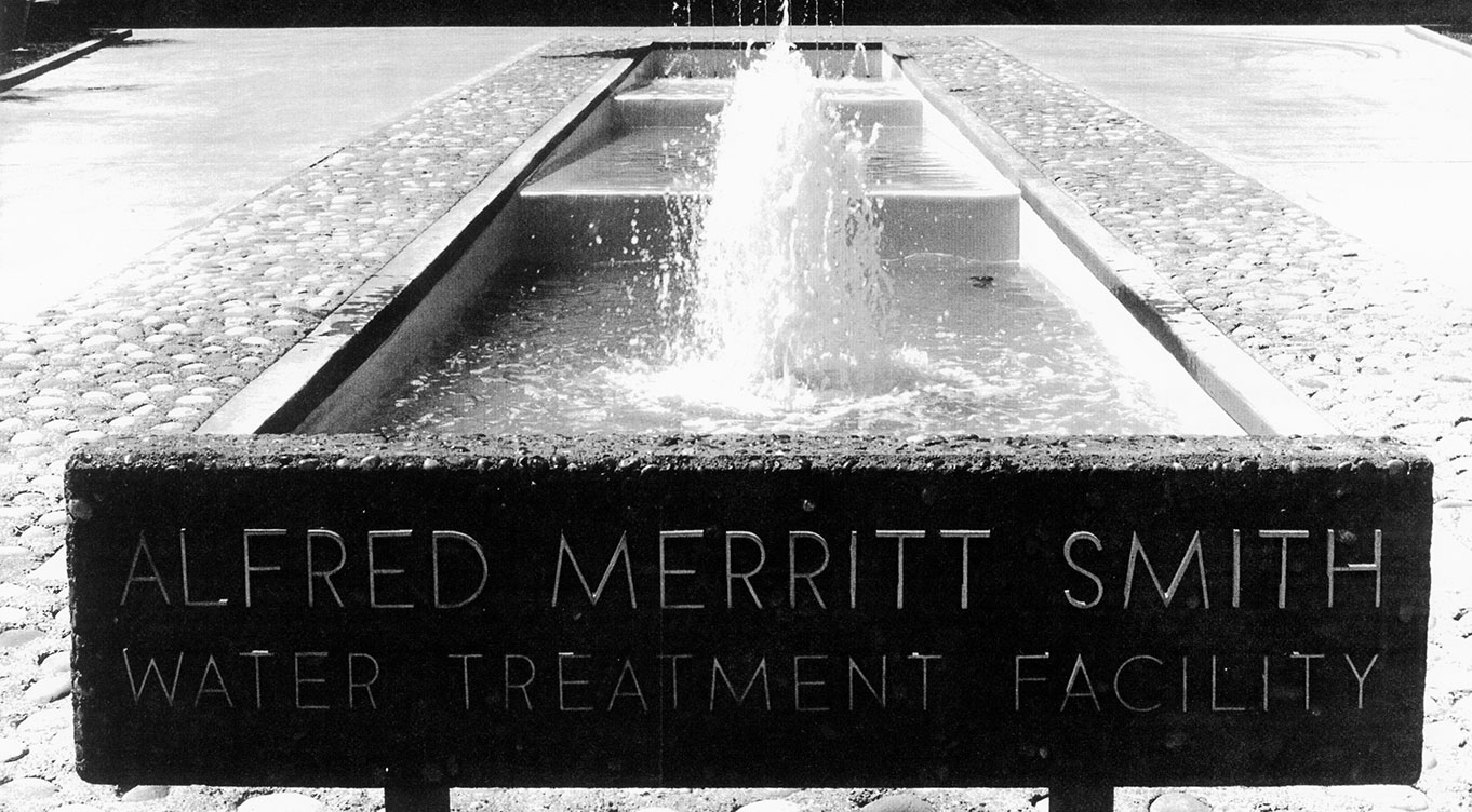 Grayscale photo of Alfred Merritt Smith Water Treatment Facility sign in front of fountain.