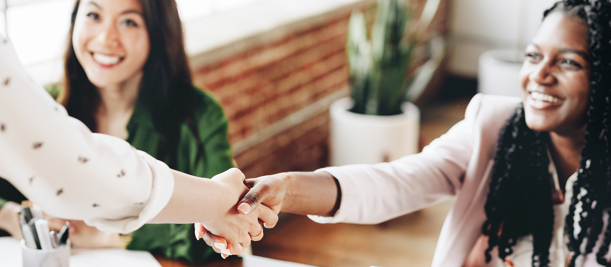 women sitting at table shake hands