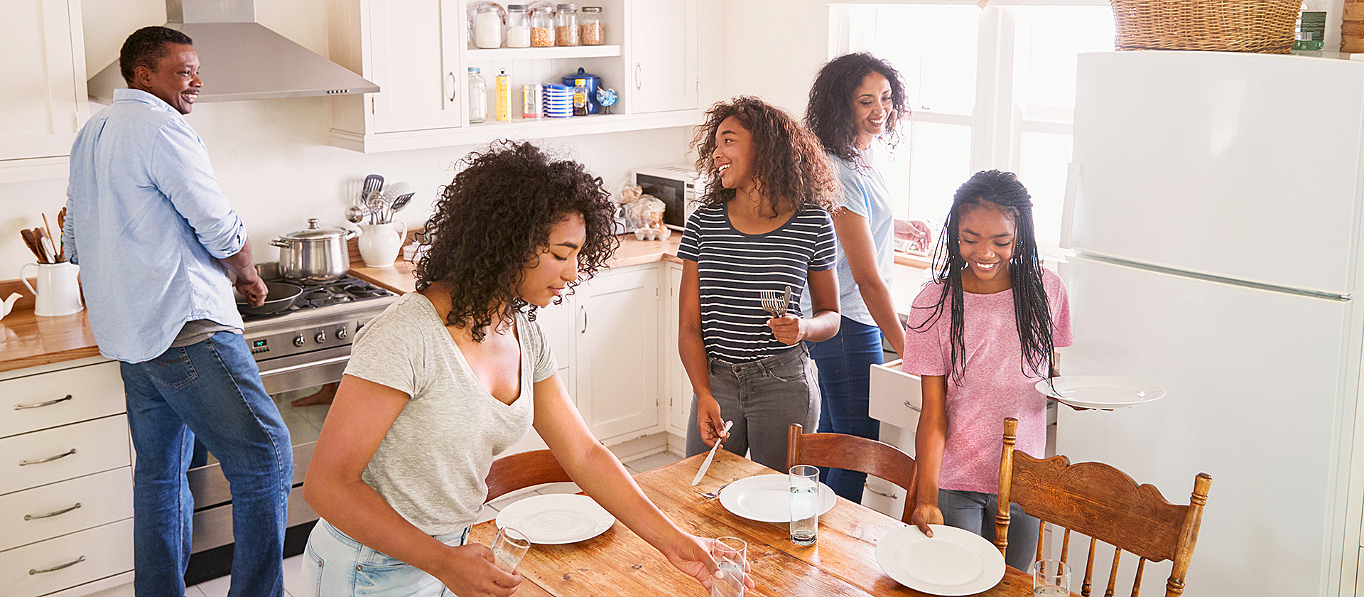 Una familia joven en una cocina poniendo la mesa.