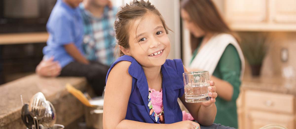 Girl drinking glass of water in kitchen with family